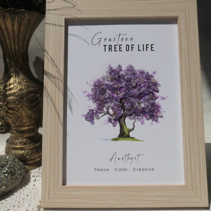 A framed art print featuring a watercolor purple flower tree with the text 'Gemstone Tree of Life' and 'Anathyst Peace, Calm, Creative'. The print is housed in a light natural wood frame and styled next to a decorative gold vase.